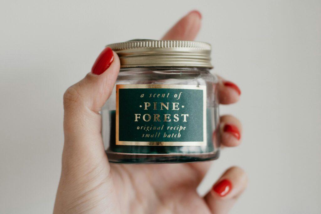 A stylish close-up of a hand holding a pine forest scented candle in a retro jar.